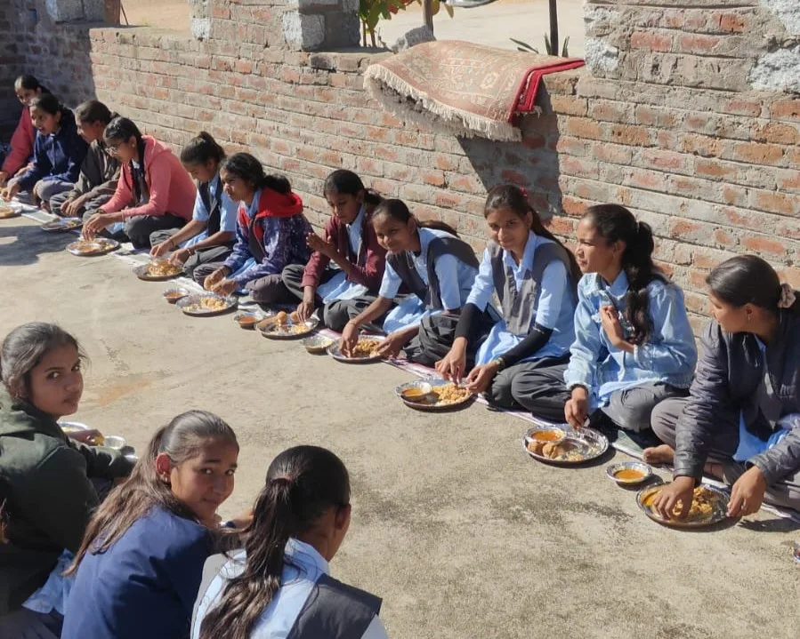 School students sitting along the wall sharing a meal at the gaushala
